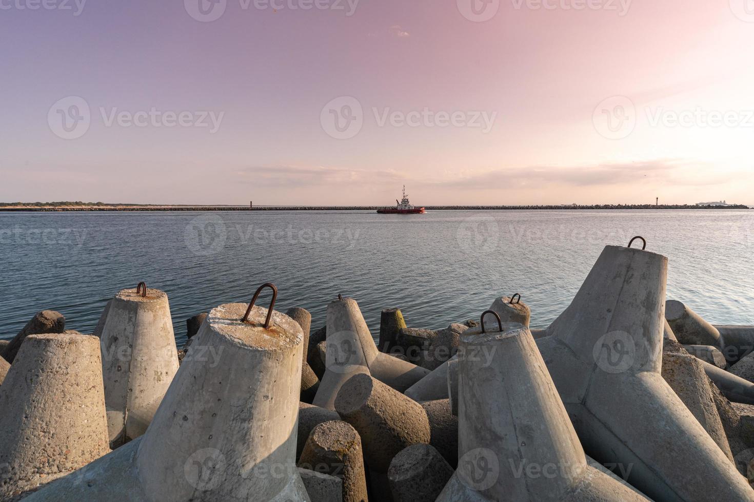 Ship-tugboat goes in high seas to tow cargo ship to port. Beautiful sunset over the pier. Tetrapod breakwaters in harbor. photo