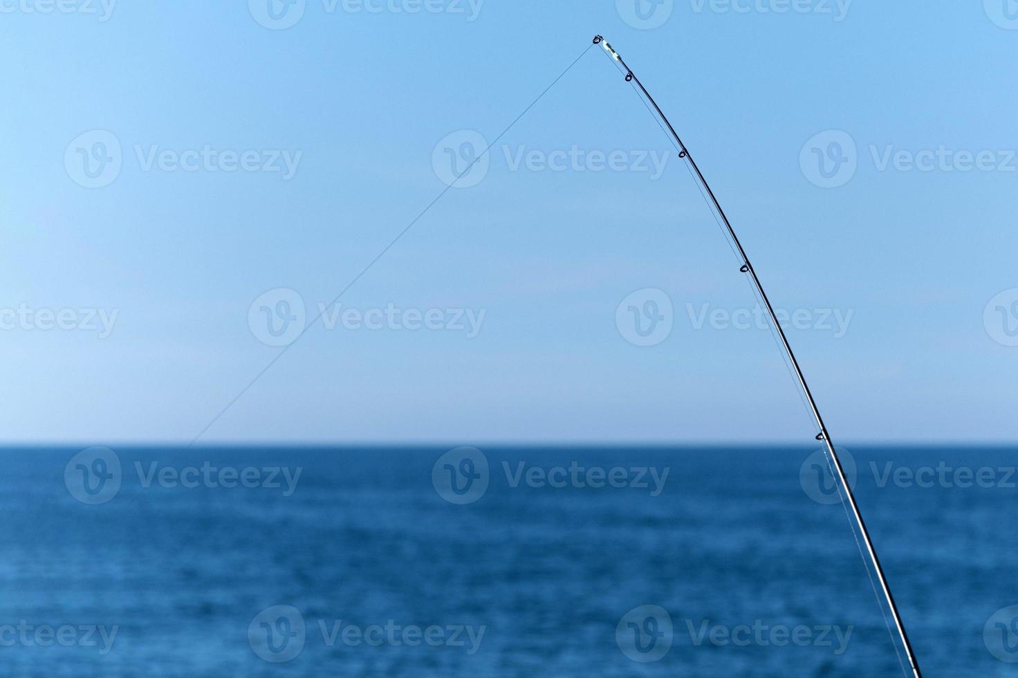 Fishing rod against blue ocean or sea background, copy space. Waiting for biggest haul. Meditative relax sport. photo