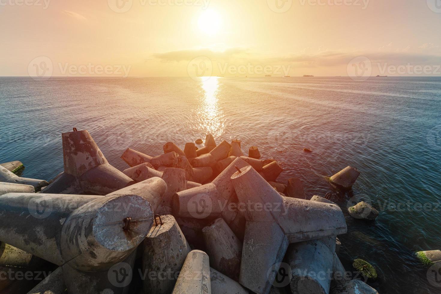 Beautiful sunset seascape. Breakwaters tetrapods ashore of pier. Cargo ships on the horizon. Travel dreams and motivation photo