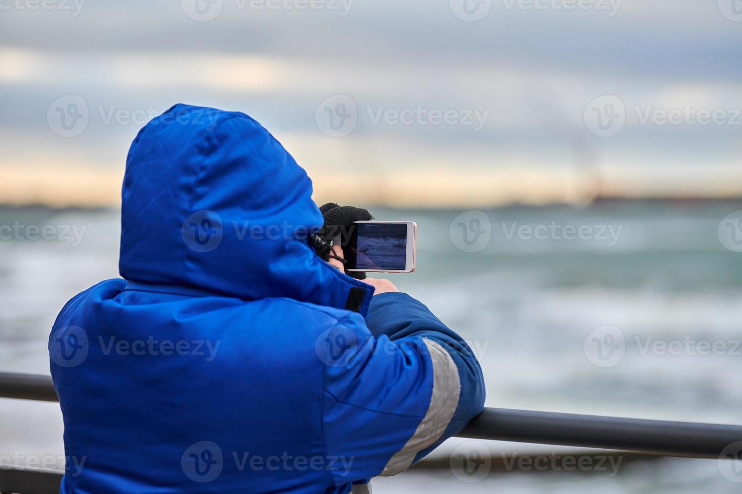 Back view of man tourist taking photo of sea with smartphone