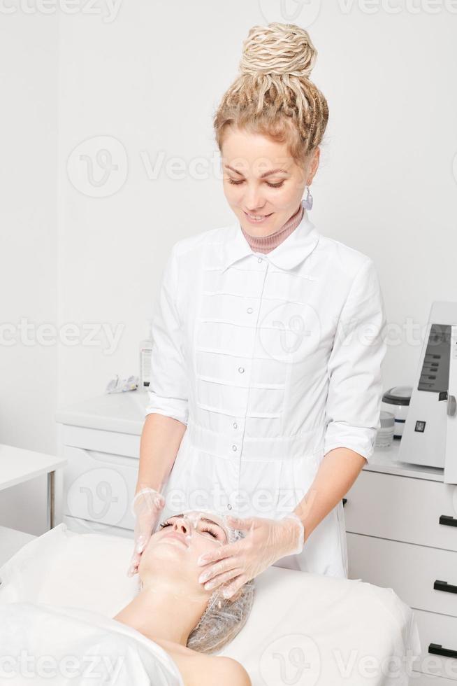 Cosmetologist massages cream mask into woman face skin for rejuvenation, procedure in beauty salon photo