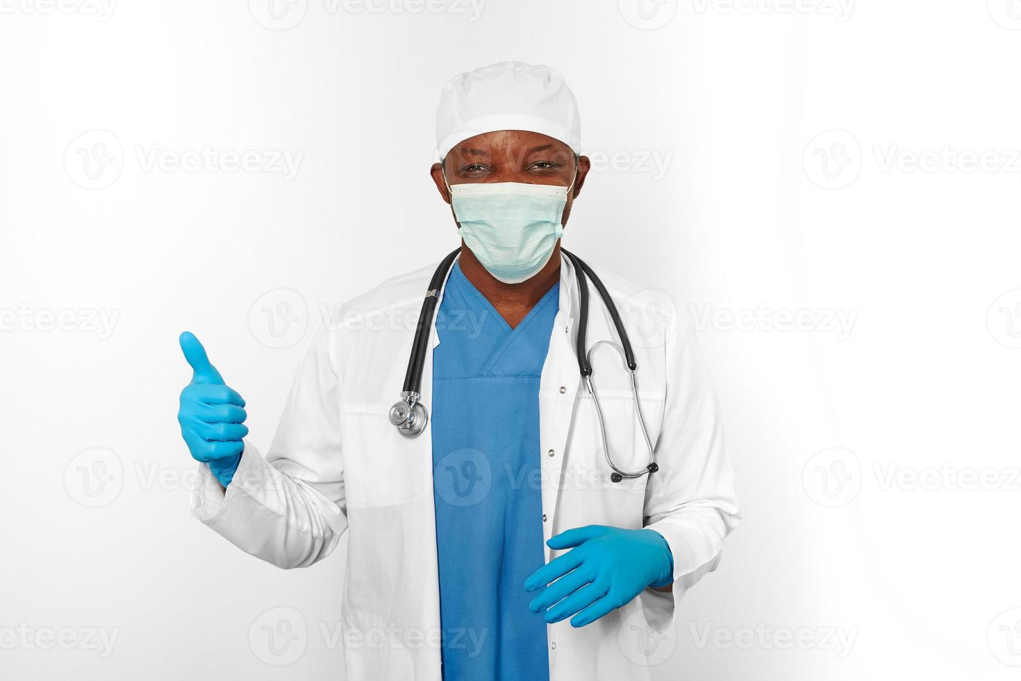 Black surgeon doctor man in white coat gloves white cap and surgeon mask makes thumbs up gesture photo