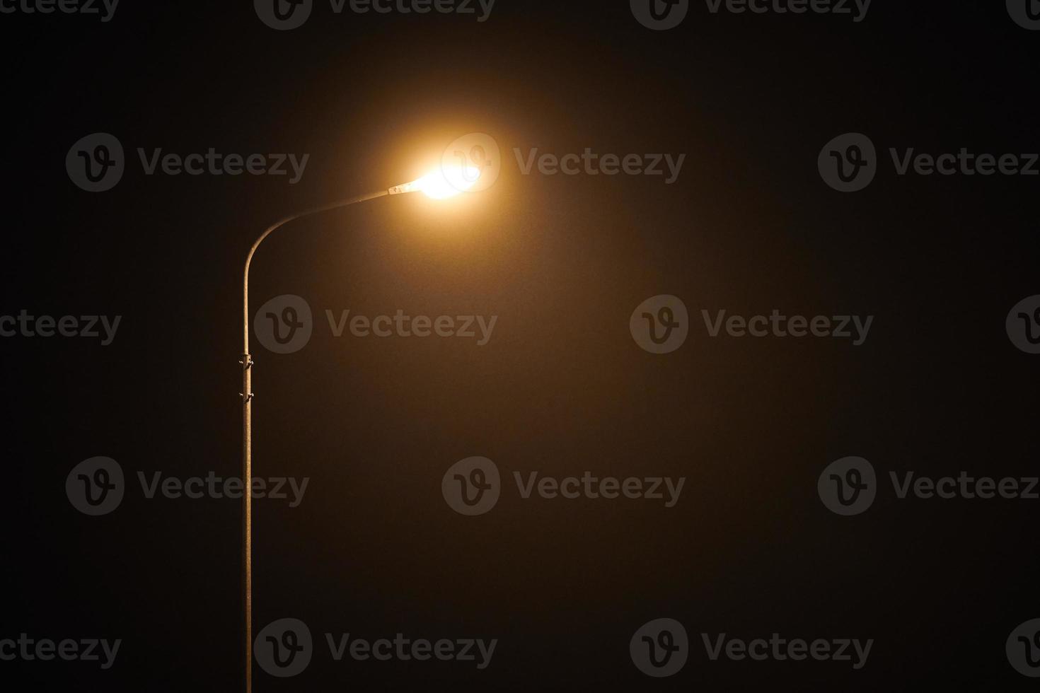 One night lamppost shines with faint mysterious yellow light through evening fog, copy space photo