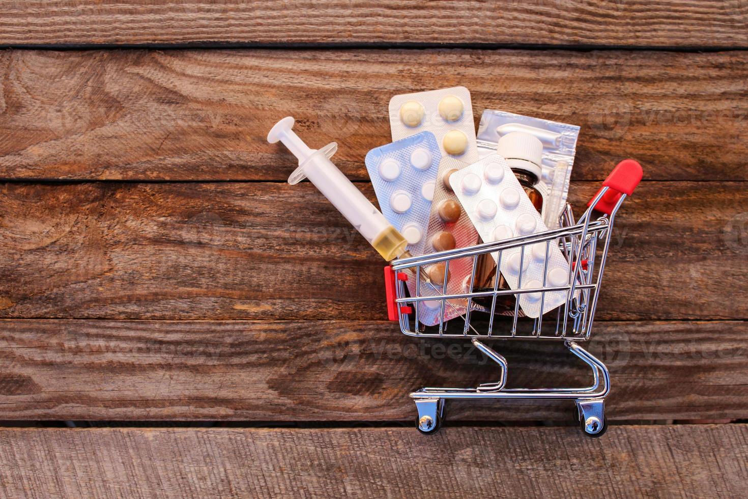 Shopping cart with pills, syringe on the old wood background. Toned image. photo