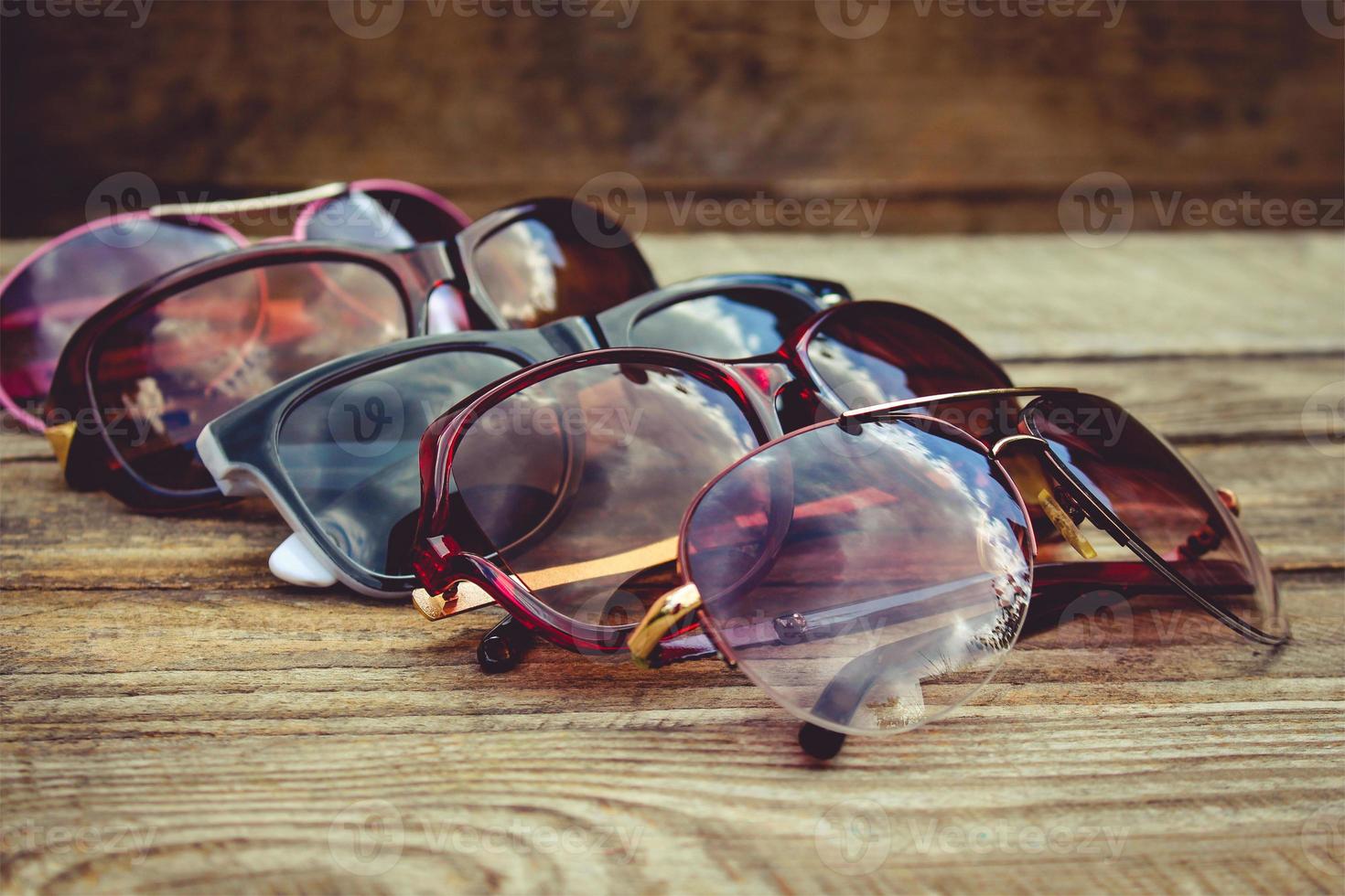 Different sunglasses on wooden background. Reflection of clouds and trees in sunglasses. Toned image. photo