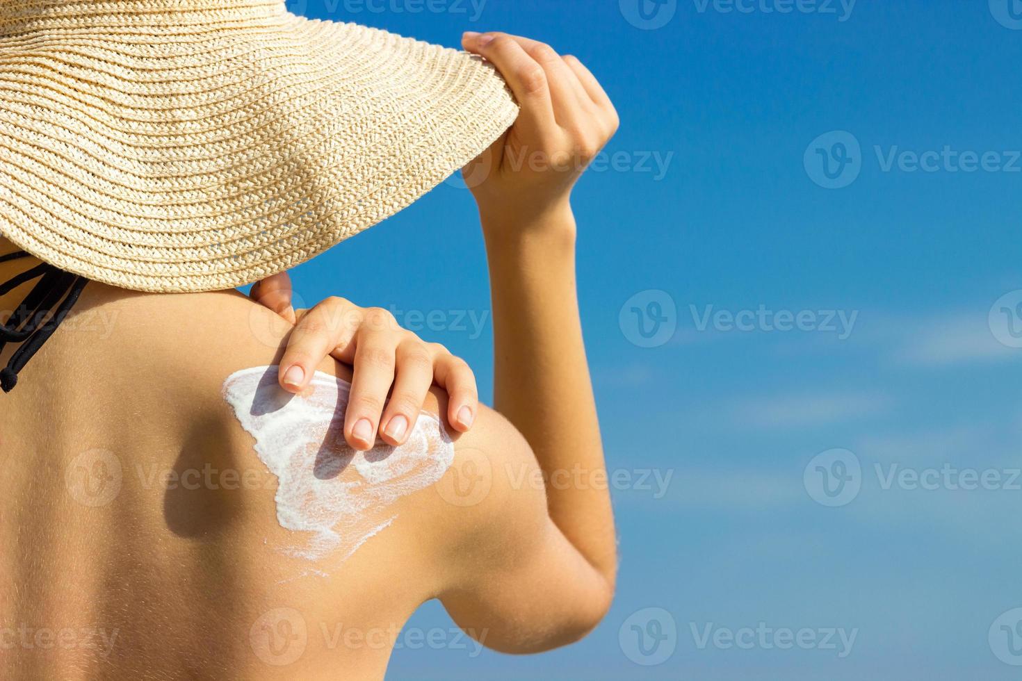 Sunscreen sunblock. Woman in a hat putting solar cream on shoulder outdoors under sunshine on beautiful summer day. photo