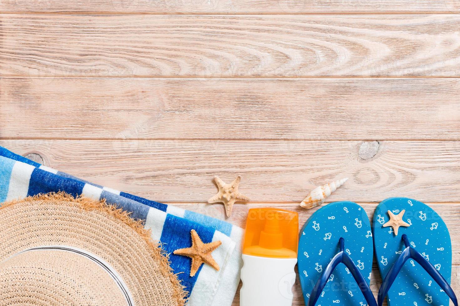 chanclas, sombrero de paja, estrellas de mar, botella de protector solar, spray de loción corporal en la vista superior de fondo de madera. fondo plano de accesorios de mar de playa de verano, concepto de viaje foto