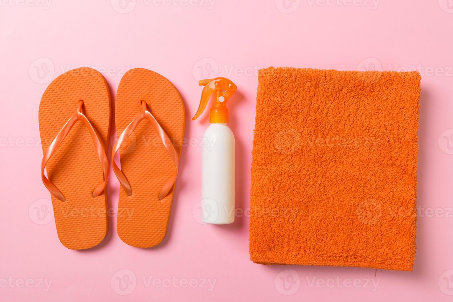 Top view of Beach flat lay accessories. sunscreen bottle with seashells, starfish, towel and flip-flop on Colored background with copy space photo