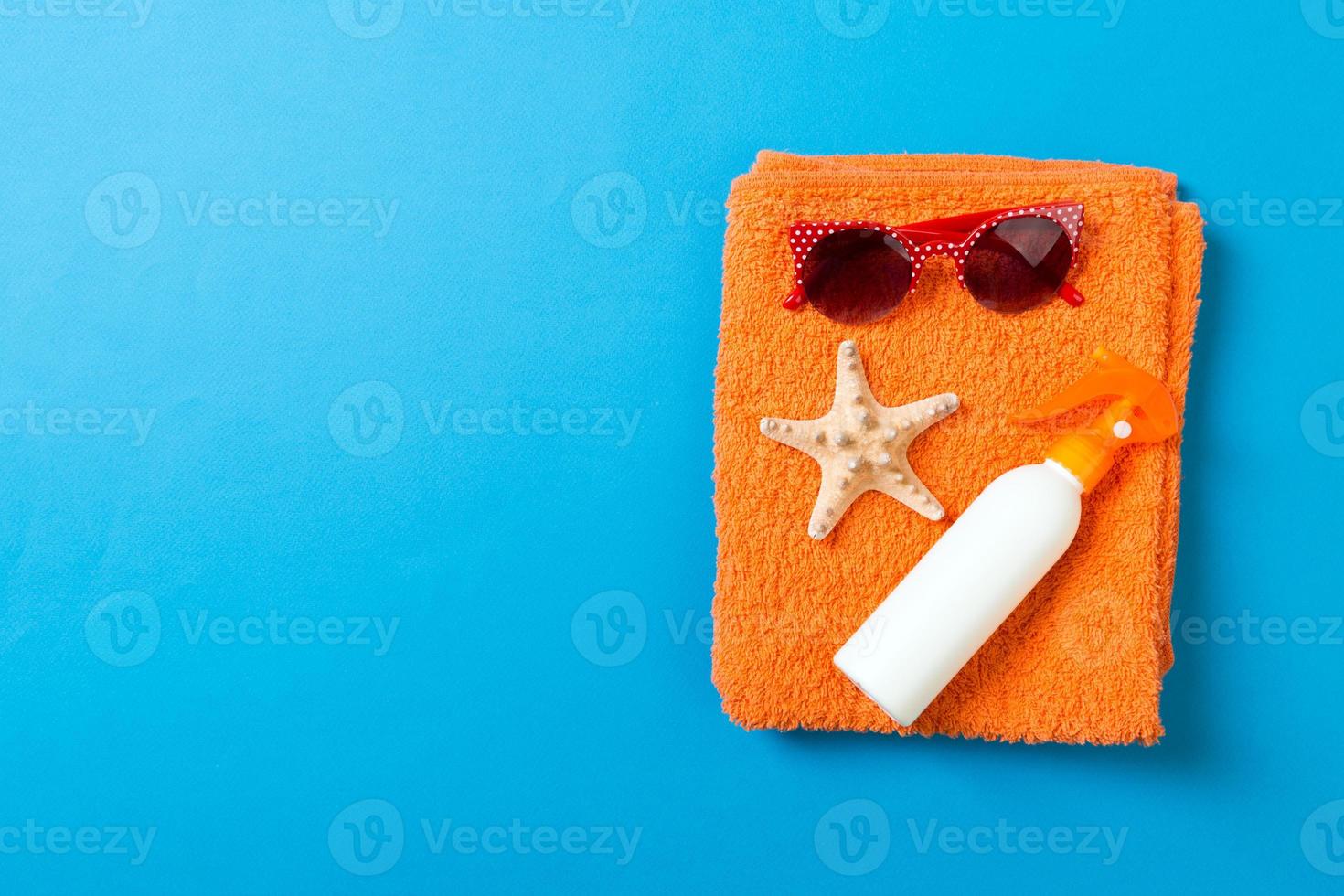 Summer beach flat lay accessories. Sunscreen bottle cream, towel and seashells on colored Background. Travel holiday concept with copy space photo
