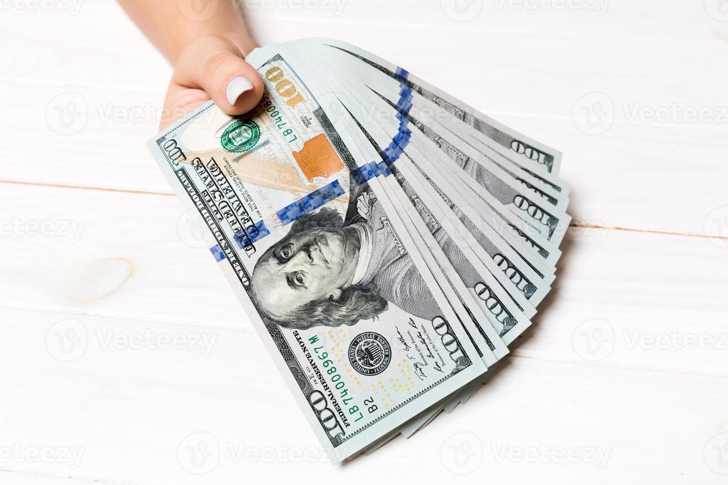 Perspective view of female hand holding a fan of money on wooden background. One hundred dollar bills. Credit and debt concept photo