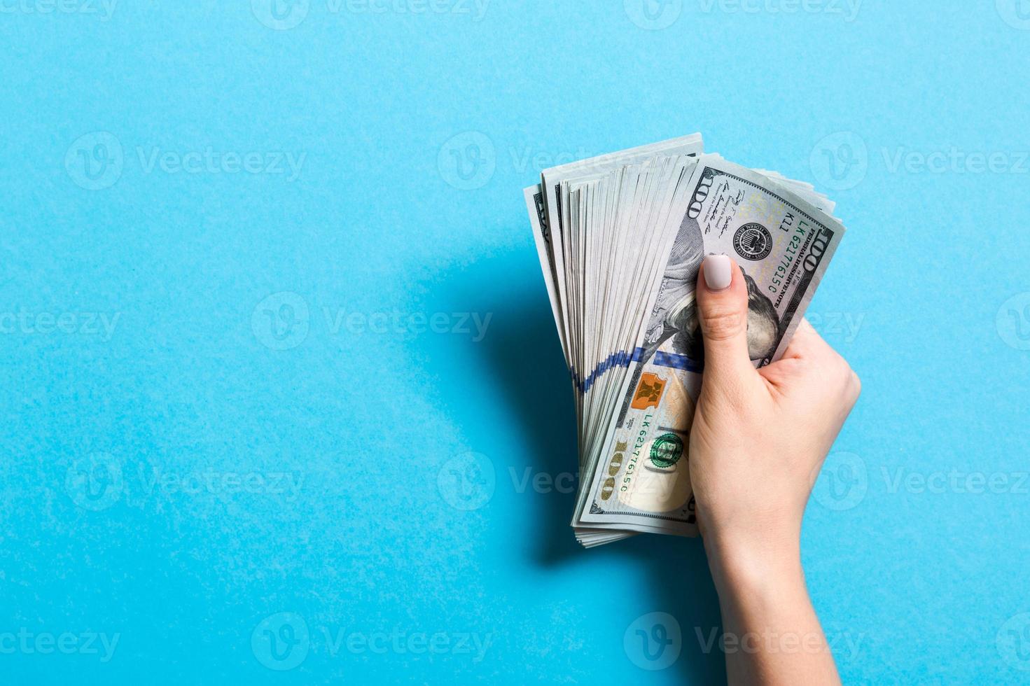 Top view of female hand holding a pack of one hundred dollar bills on colorful background. Wage and salary concept with empty space for your design photo
