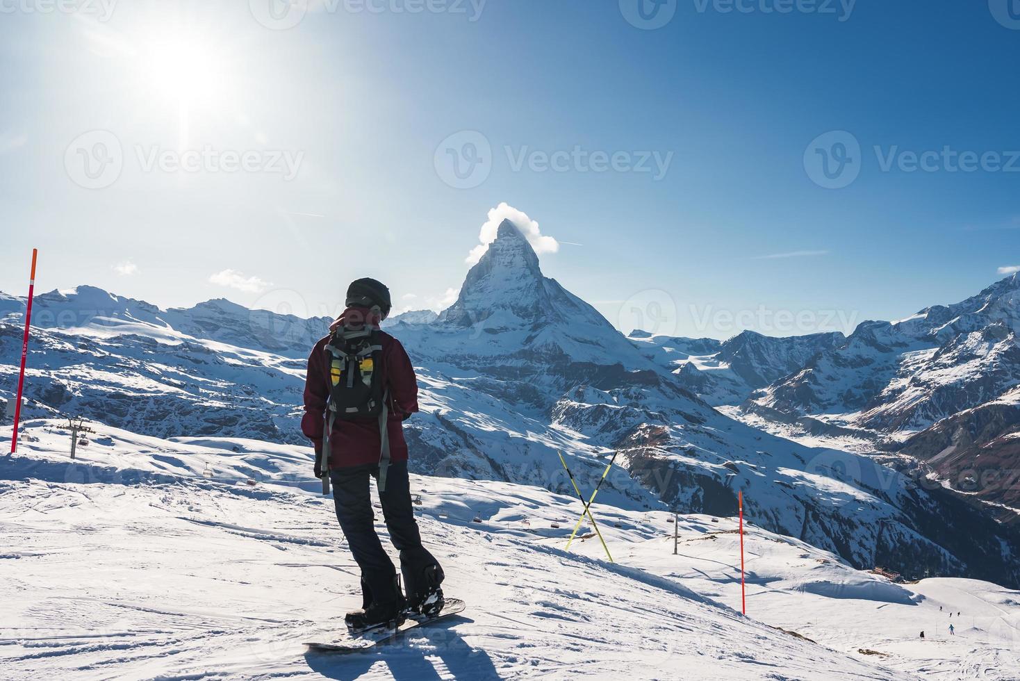 Young man snowboarding in Zermatt ski resort right next to the famous Matterhorn peak. Beautiful sunny day for snowboarding. Winter sports concept. photo