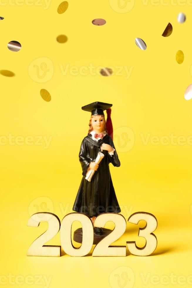 Class of 2023 concept. Wooden number 2023 with graduate statuette on color background with flying tinsel photo