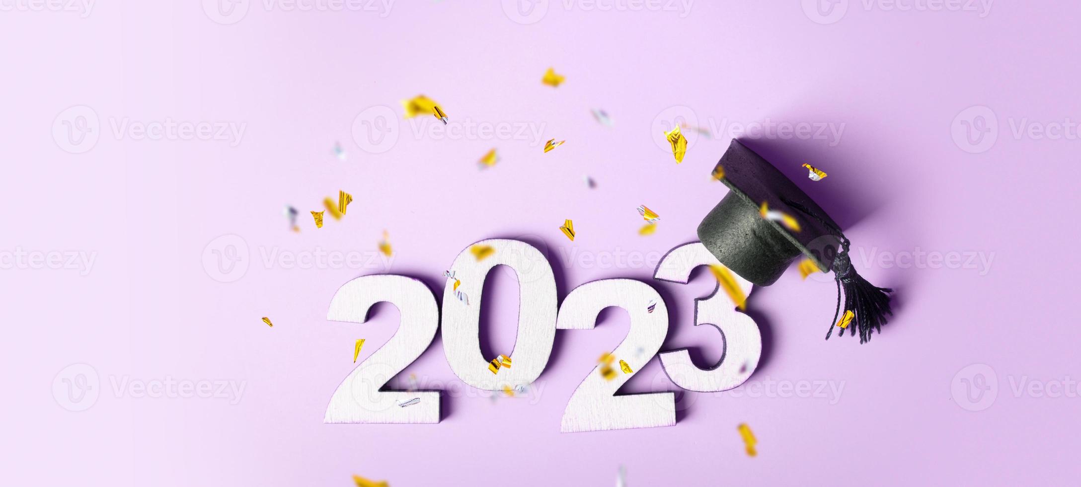 Class of 2023 concept. Wooden number 2023 with graduated cap on colored background with flying tinsel photo