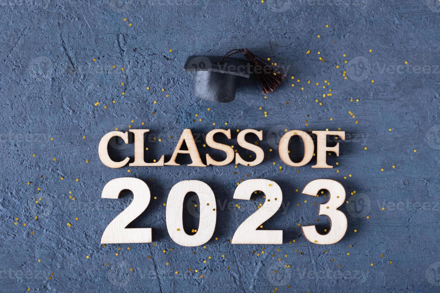 Class of 2023 concept. Wooden number 2023 with graduate hat on dark background with tinsel photo