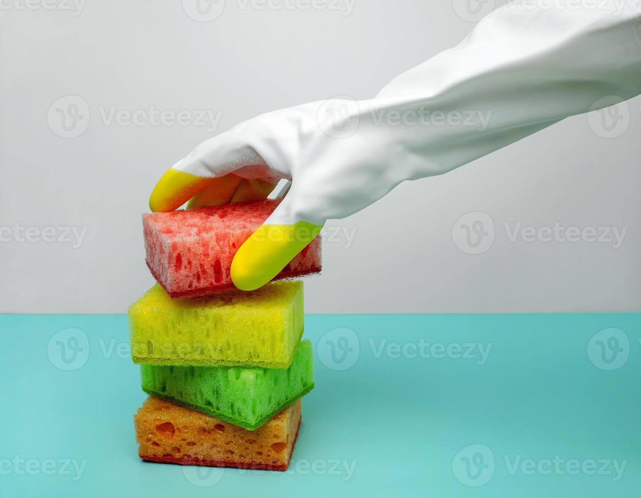 The concept of cleanliness. A gloved hand picks up washing-up sponge on a blue background. Spring cleaning of the house photo