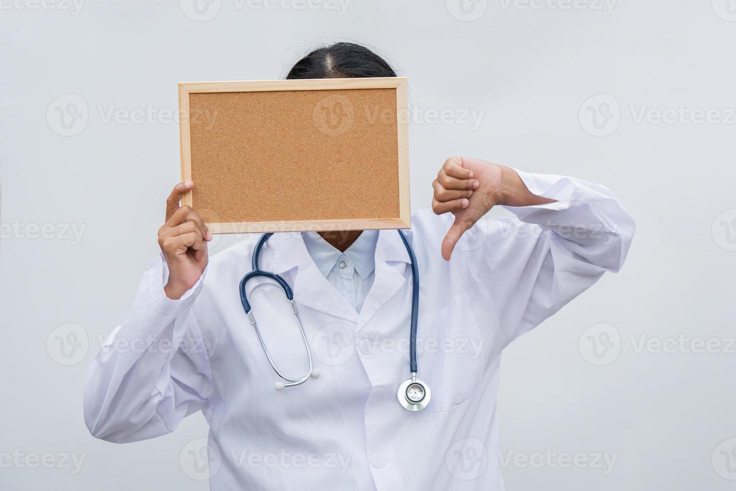 professional female doctor in white coat over white isolated background and white blank board and Thumbs down. Concept of healthcare, science and medicine concept photo