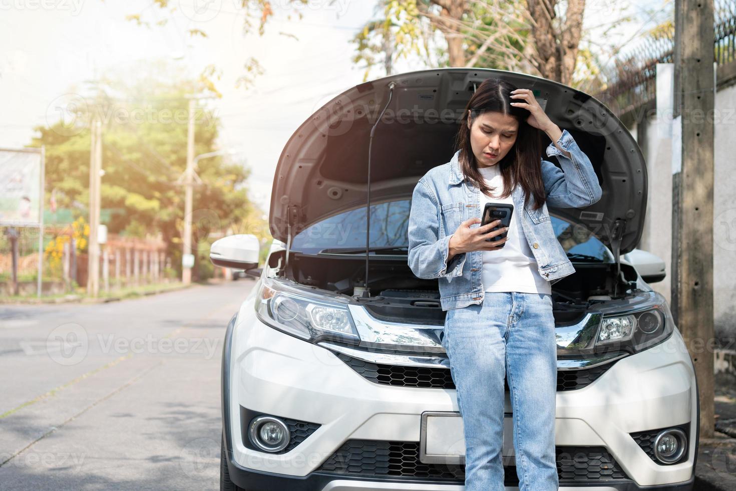 mujer asiática enojada y usando un teléfono móvil pidiendo ayuda después de una avería en el coche en la calle. concepto de problema del motor del vehículo o accidente y ayuda de emergencia de un mecánico profesional foto