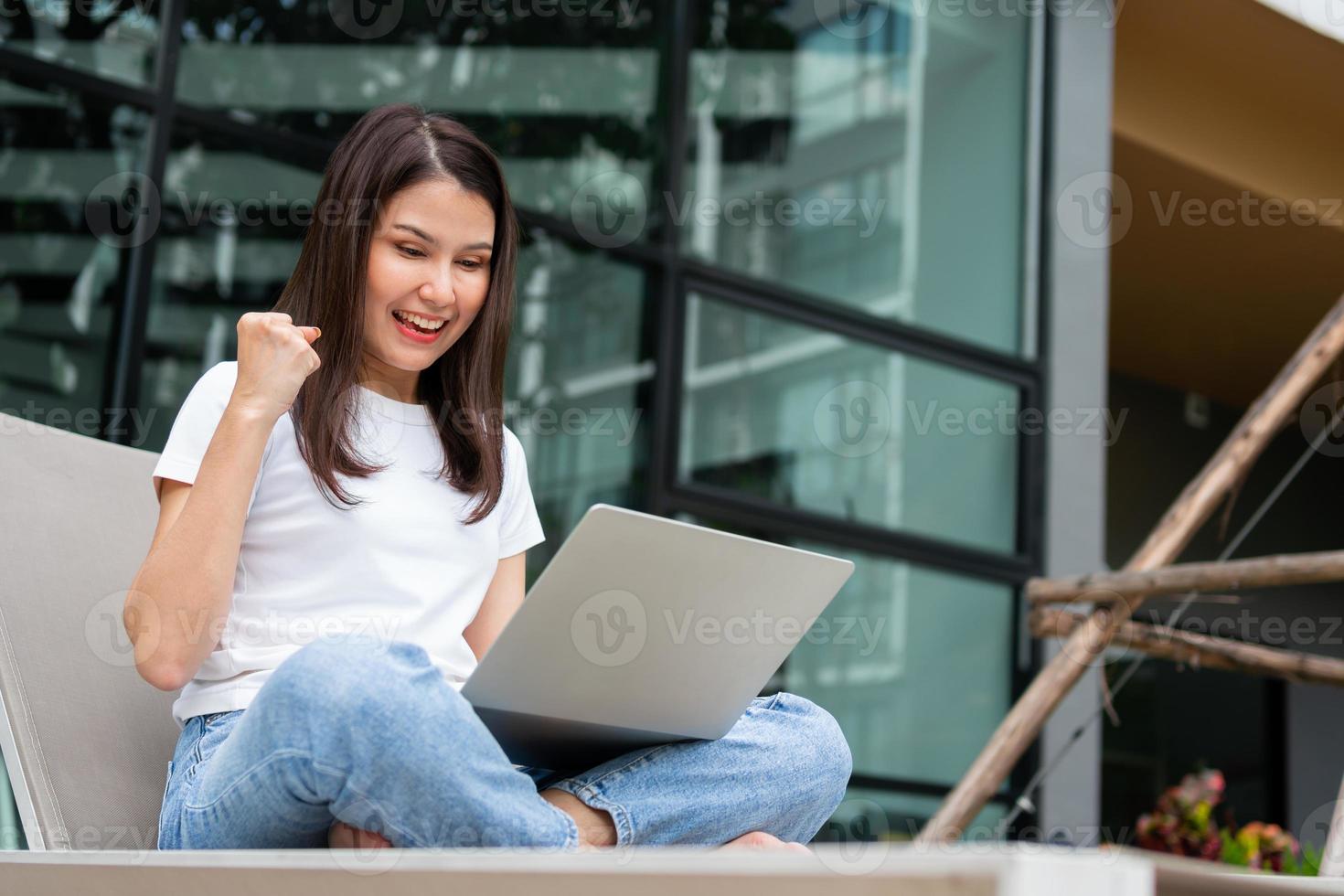 feliz joven empresaria sentada en una cama de bronceado junto a la piscina y usando una computadora portátil para trabajar en línea a distancia digital, proyecto de negocios en línea en un patio tranquilo de una casa de vacaciones, trabajar de vacaciones foto