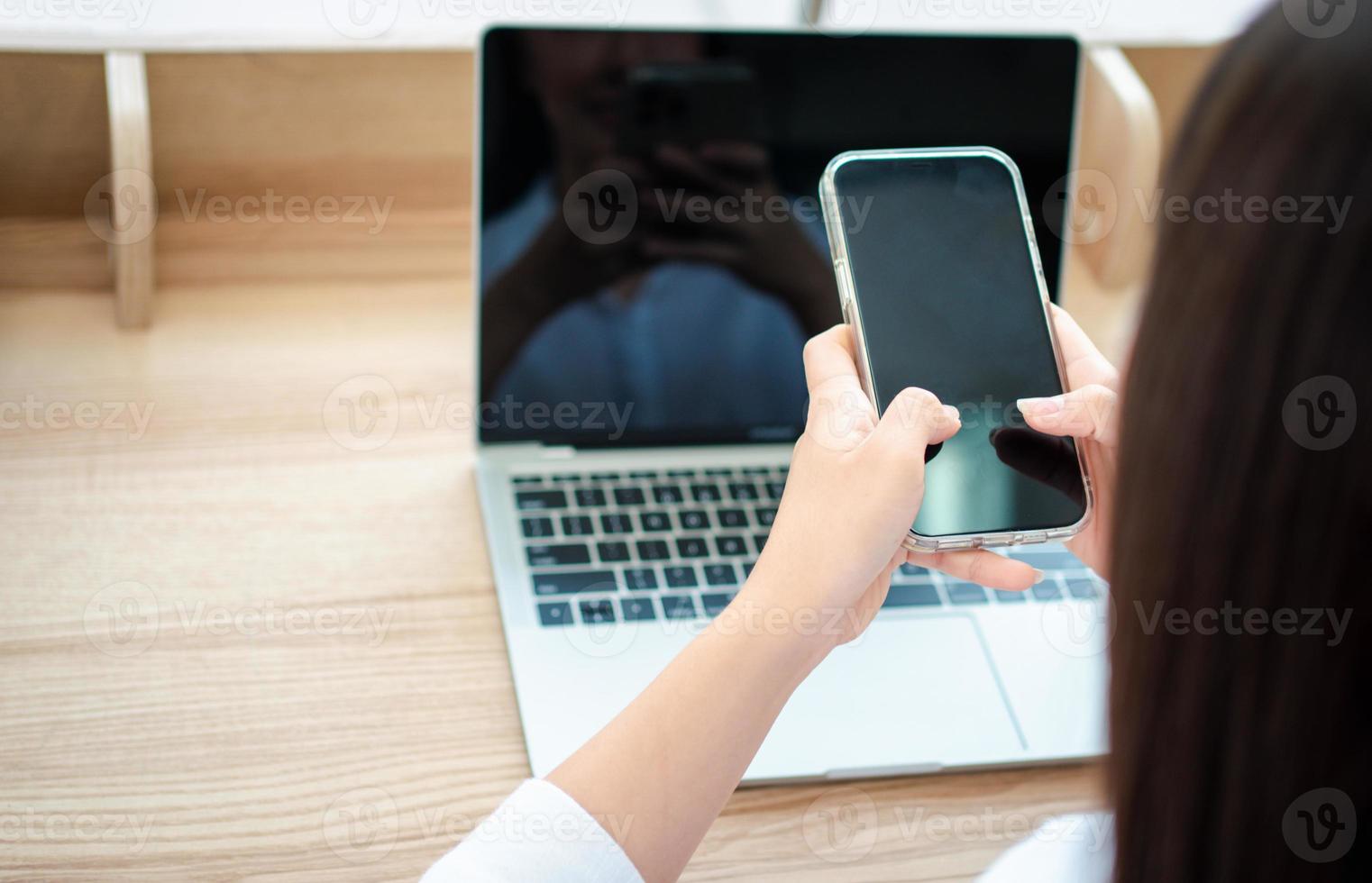 Happy beautiful asian woman working on a laptop and smartphone at the home office sitting at table. Happy female professional freelancer online using notebook pc and smartphone concept. photo