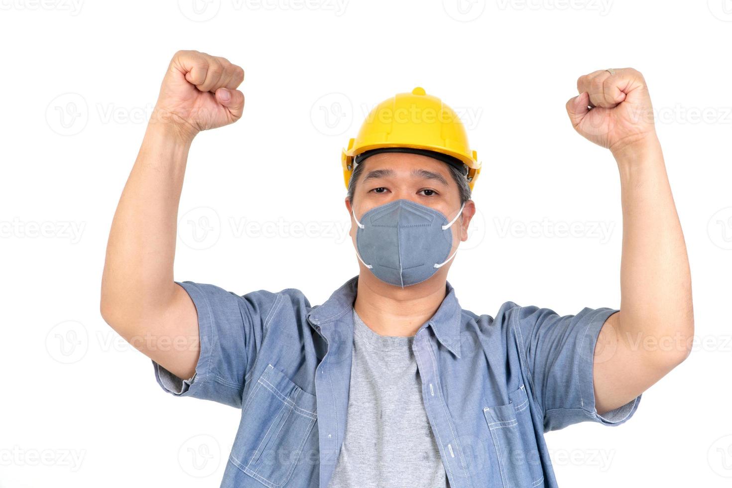 Male worker wearing a helmet and face mask and looking at camera in studio on isolated white background. Concept of protection from coronavirus COVID-19. photo