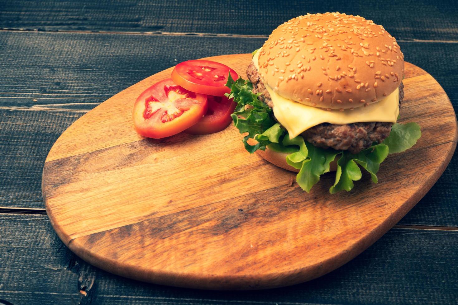 hamburguesa casera fresca y sabrosa con verduras frescas, lechuga, tomate, queso junto a rodajas de tomate en una tabla para cortar. espacio libre para texto foto