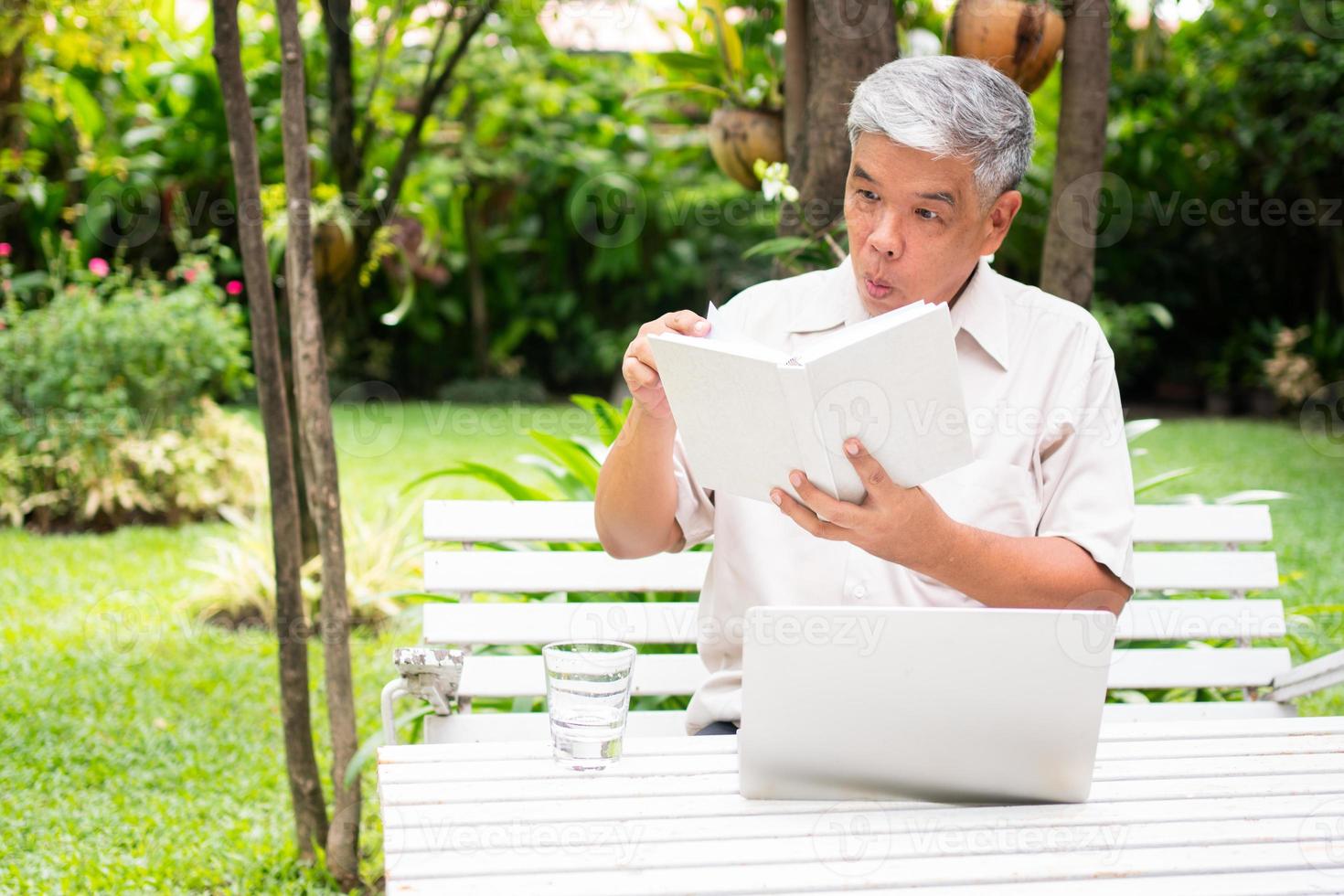 senior old man reading a book in the park and drinking water. Concept of retirement lifestyle and hobby. photo