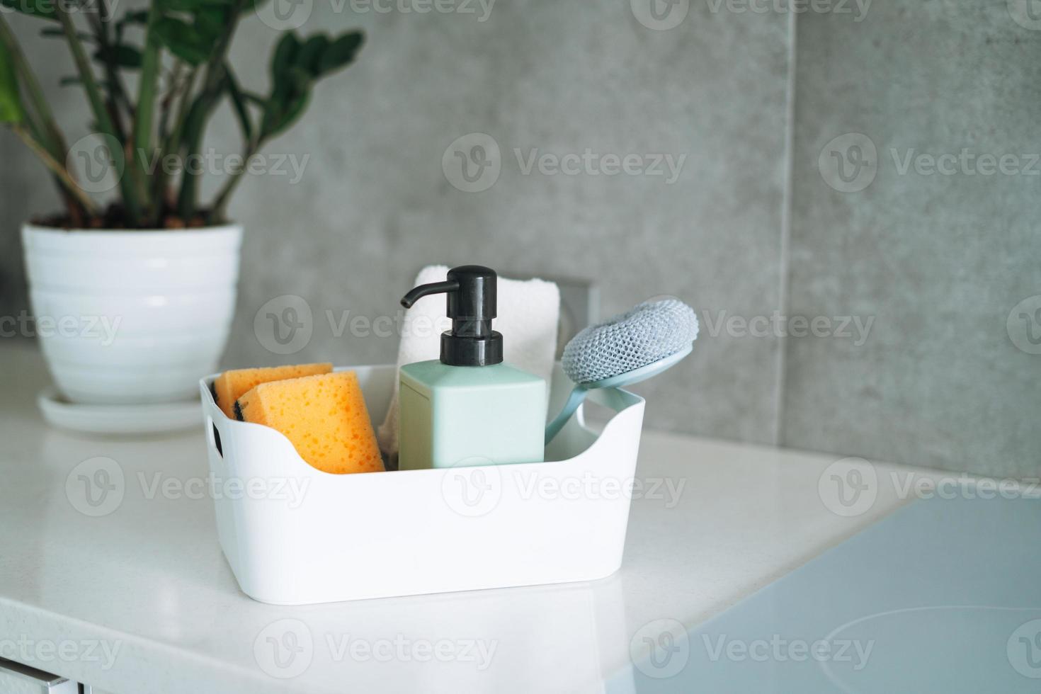 Kitchen cleaning supplies brush, liquid soap, dish sponge in container on kitchen counter at home photo