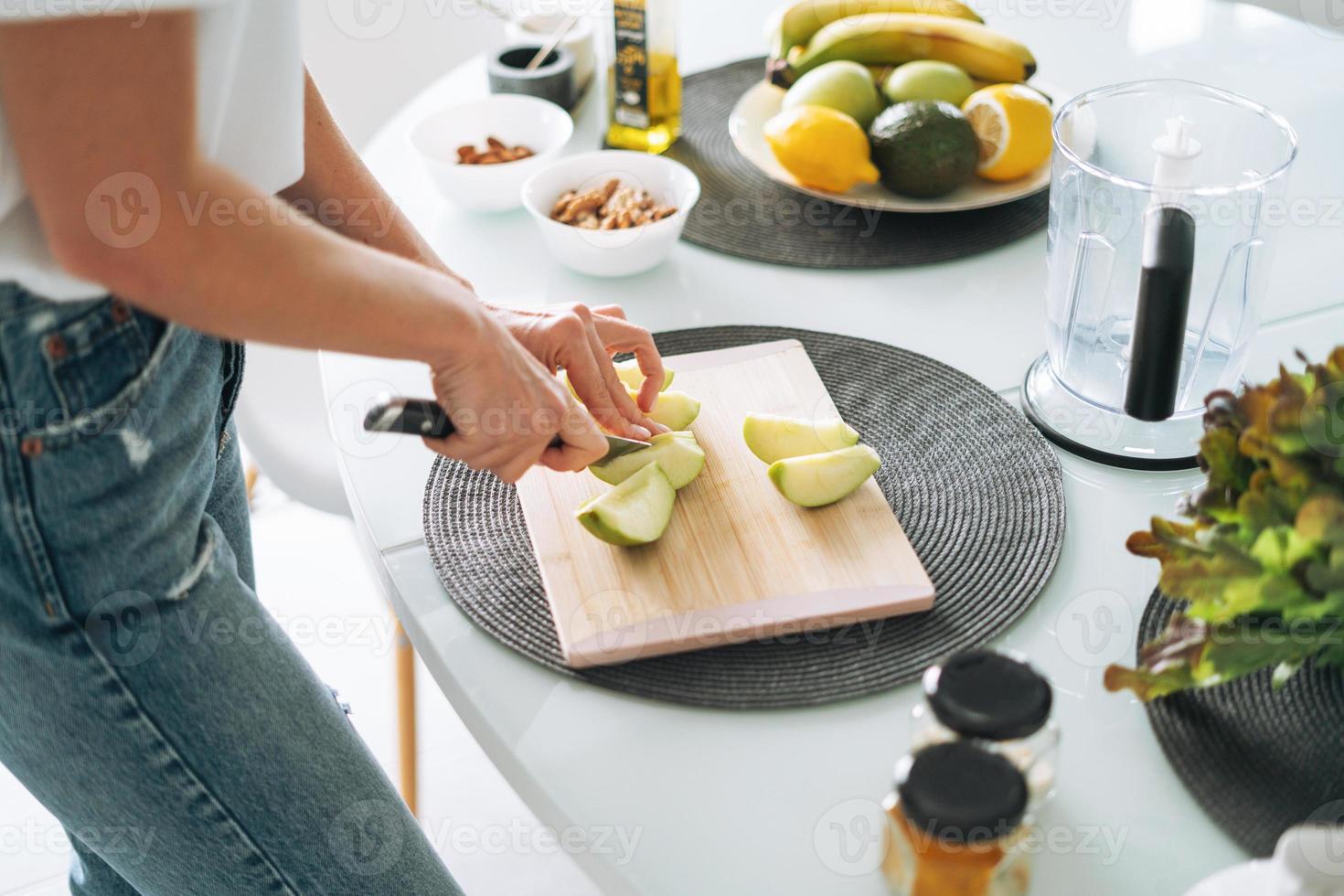 Young slim woman in white t-shirt and blue jeans cooking smoothie with apples healthy food in kitchen at home photo