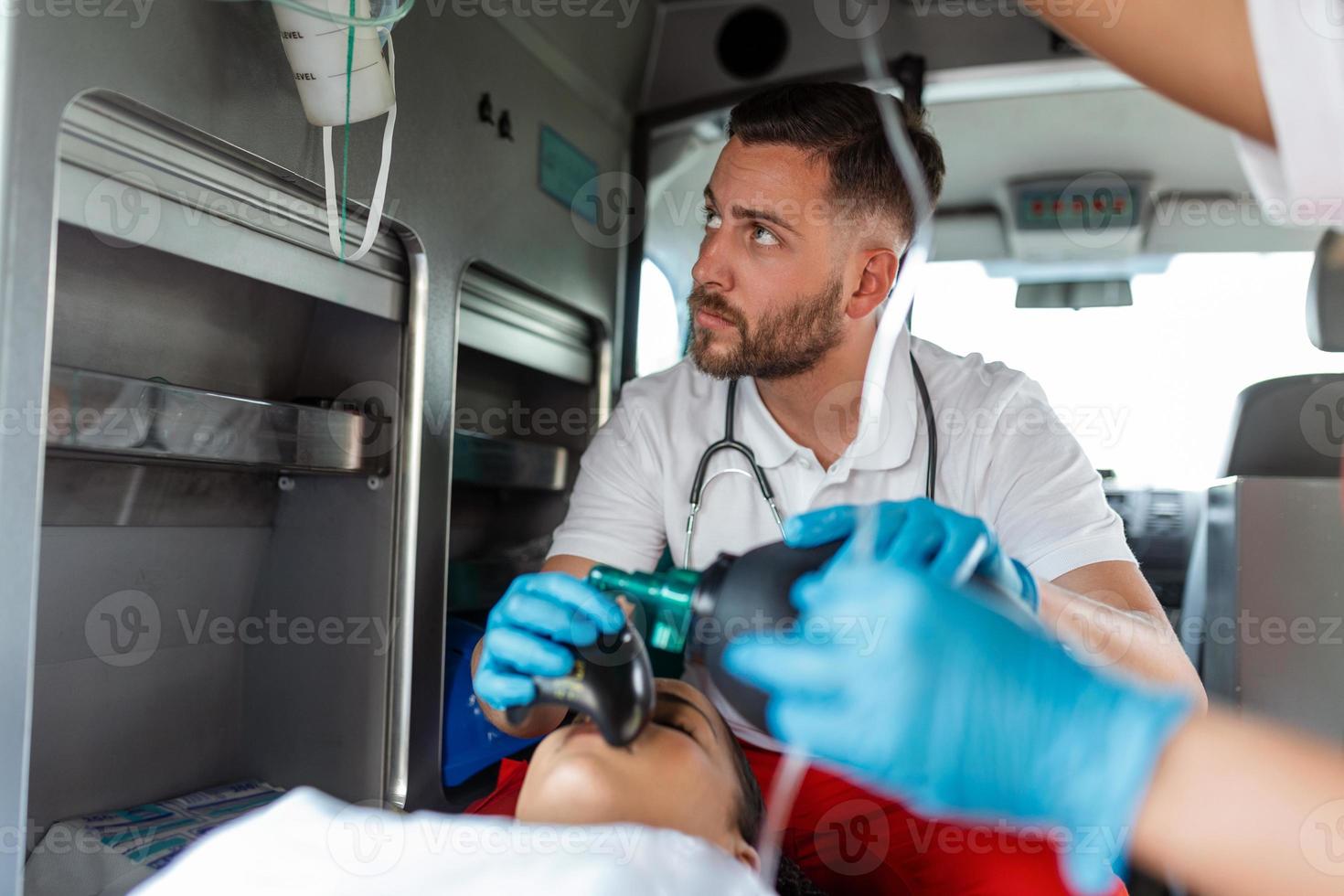 ems paramédicos equipo proporcionar médico ayuda a lesionado paciente en el camino a cuidado de la salud hospital. emergencia cuidado asistente utilizando un no invasivo ventilación máscara en un ambulancia. de cerca disparo. foto