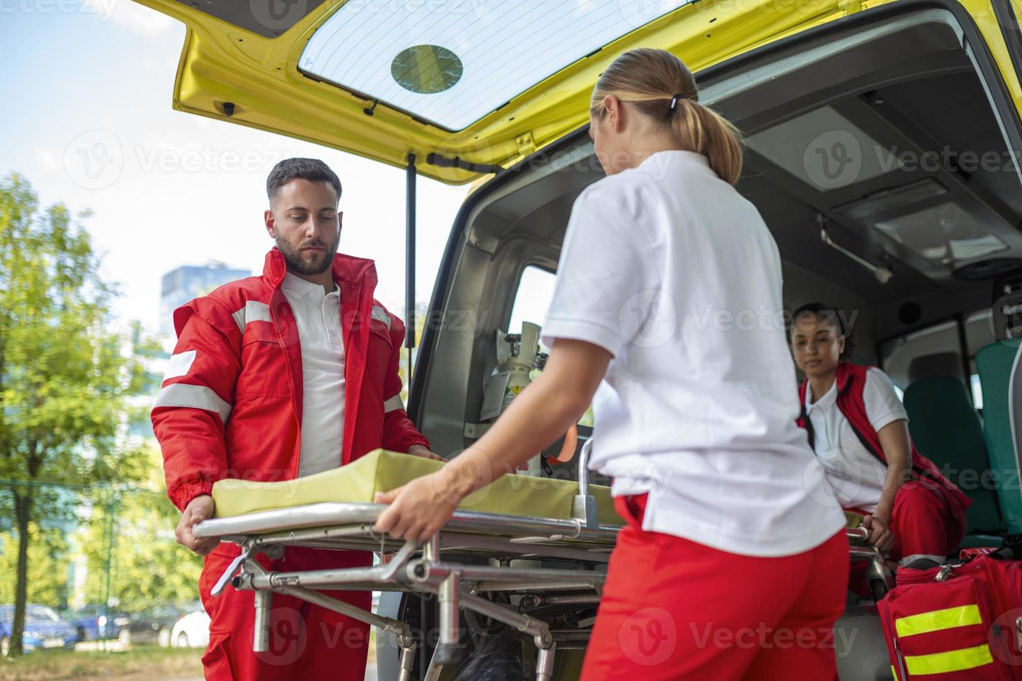 Paramedics with a stretcher near an ambulance. Paramedics in uniform taking stretcher out the ambulance car photo