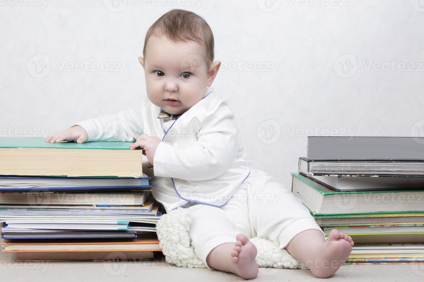 Little child among books. Happy six month old baby boy in a stack of books. The concept of early childhood education. photo