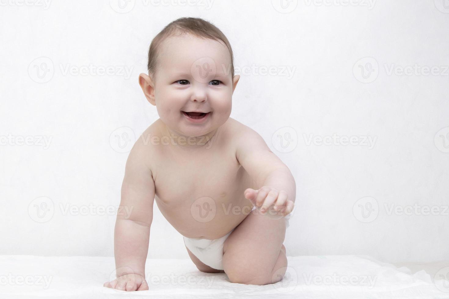 Kid with a smile on a white background. A happy six month old boy crawls on the bed and laughs. Conceptual photo of fatherhood and motherhood.