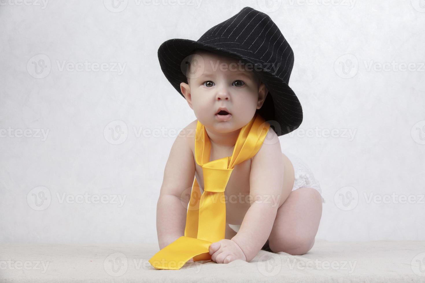 Smiling kid in a retro hat and tie on a white background. Funny six month old baby in elegant clothes. photo