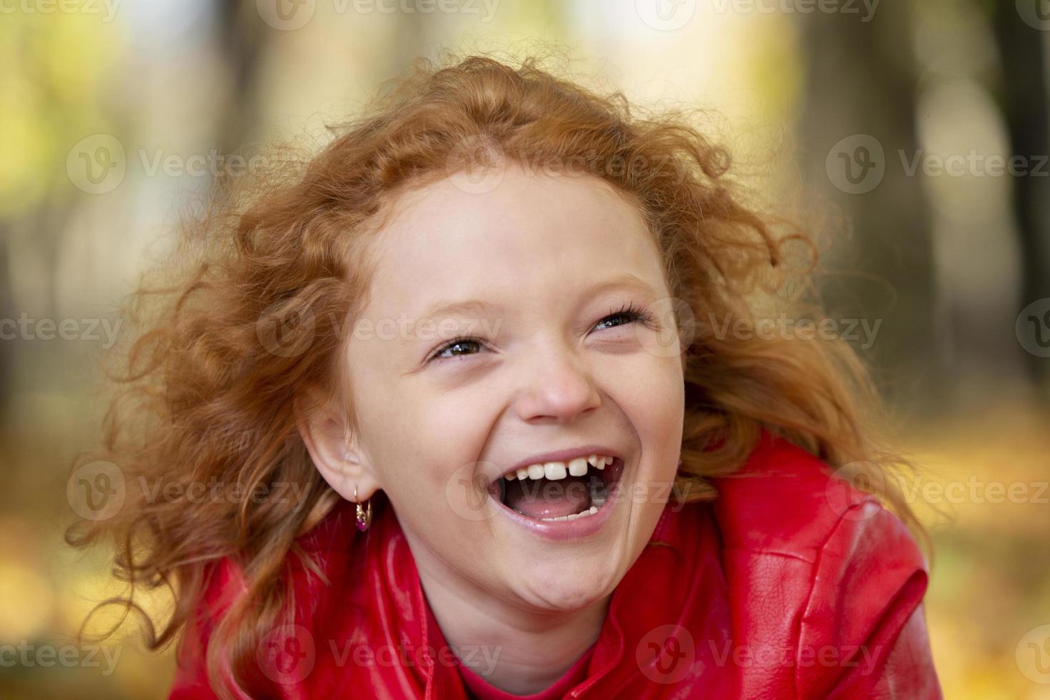 alegre Pelirrojo niña riendo alegremente en contra el fondo de un otoño parque. foto