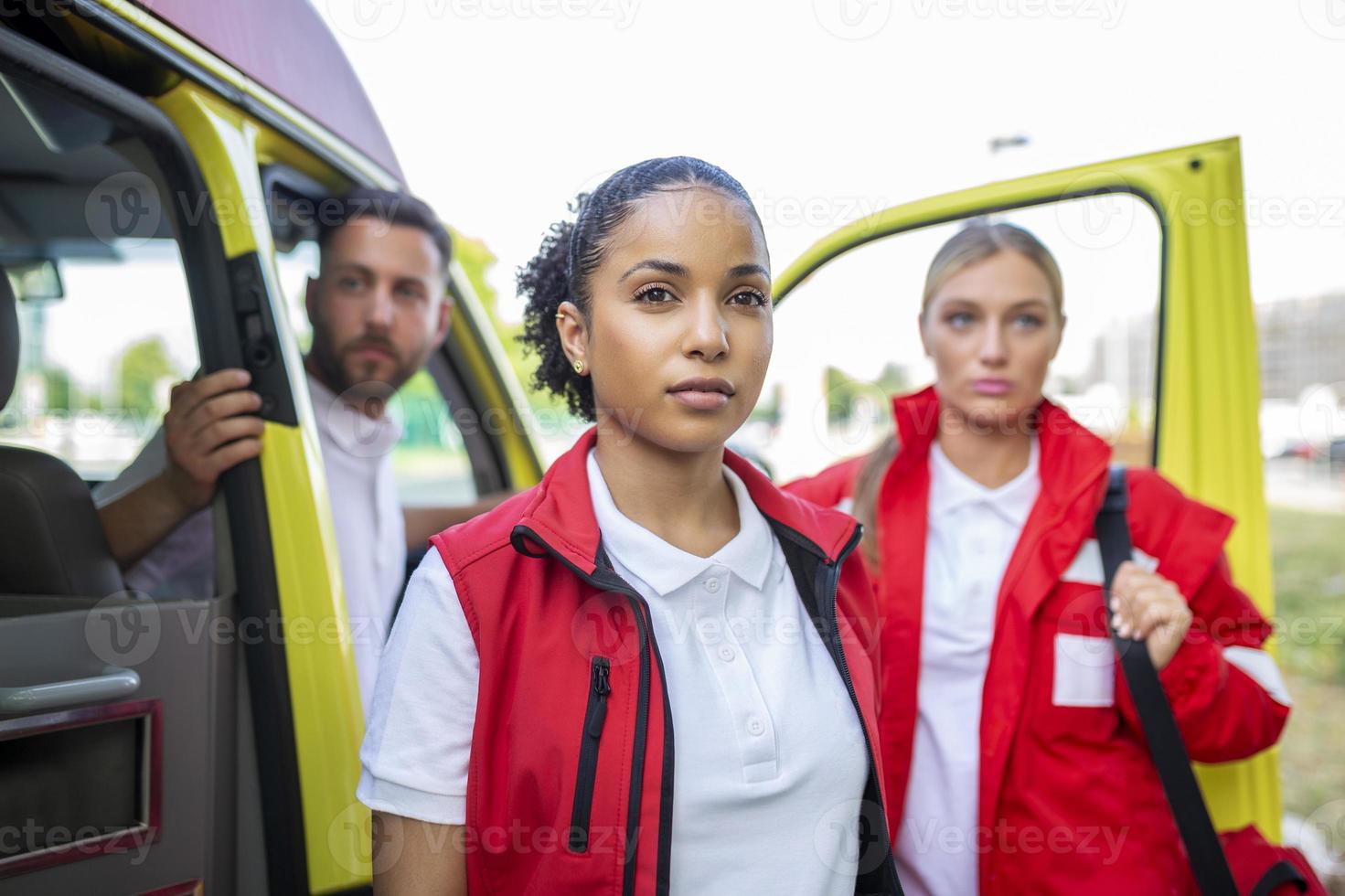 Paramedics and doctor standing on the side ambulance. Doctor is carrying a medical trauma bag. Group of three paramedics standing in front of ambulance with smile. photo