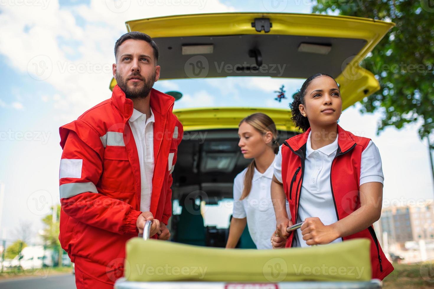 paramédicos con un camilla cerca un ambulancia. paramédicos en uniforme tomando camilla fuera el ambulancia coche foto