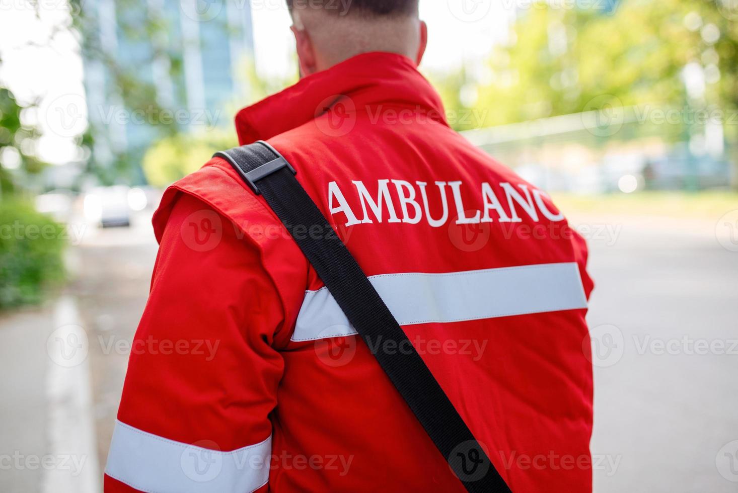 Ambulance staff member from the back with his emergency backpack , and vital signs monitor. Ambulance written on his back. photo
