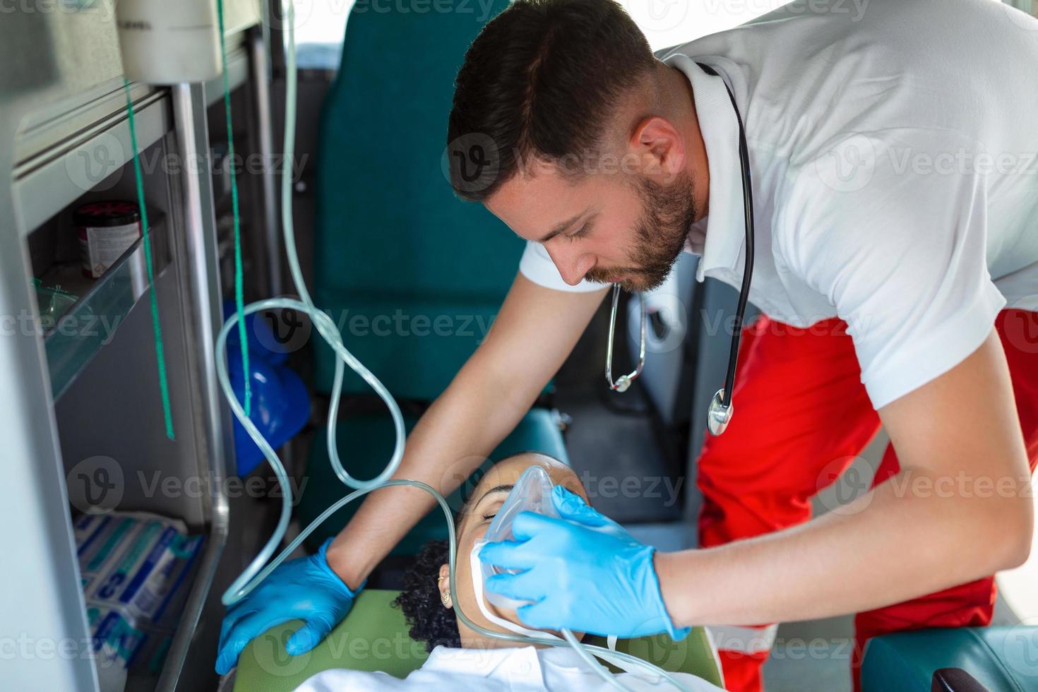 paramedic healthcare emergency staff taking care of a lying down young woman patient on stretcher with medical ventilator system and bag-valve masks inside an medical service ambulance car. photo