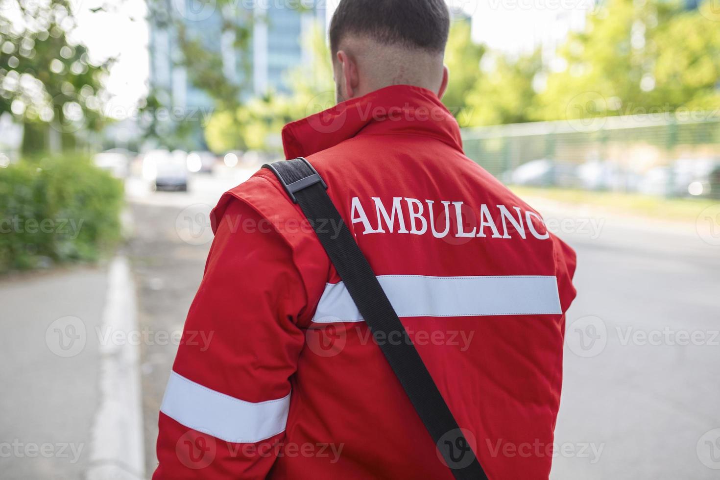 Ambulance staff member from the back with his emergency backpack , and vital signs monitor. Ambulance written on his back. photo