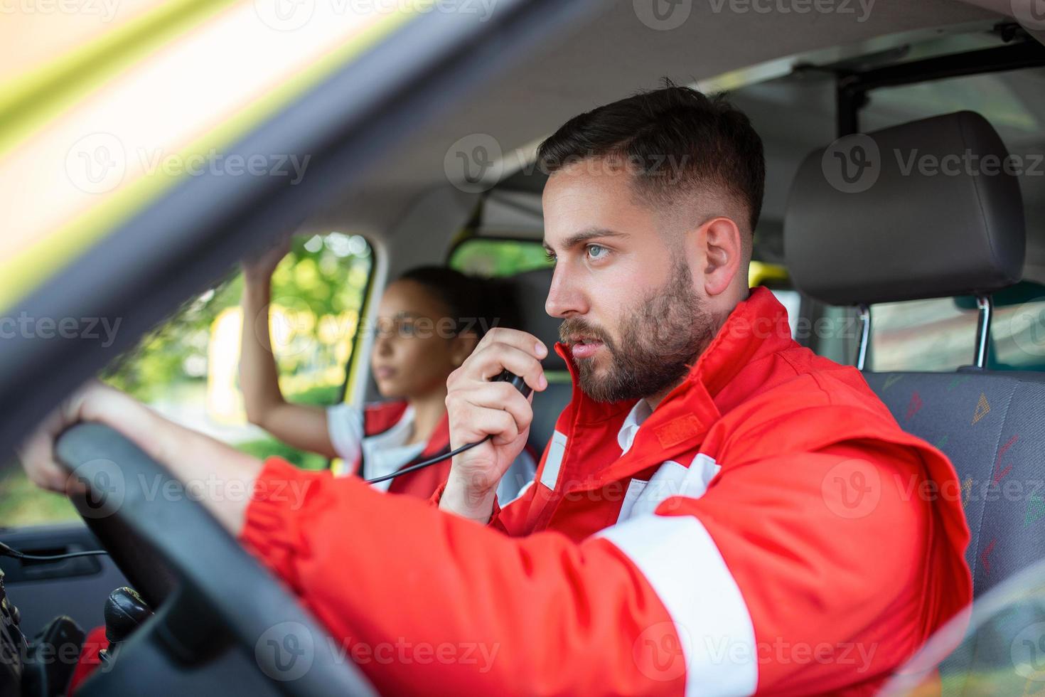 Urgent situation. Two young paramedics in ambulance. Male, caucasian paramedic driving and talking over the radio photo