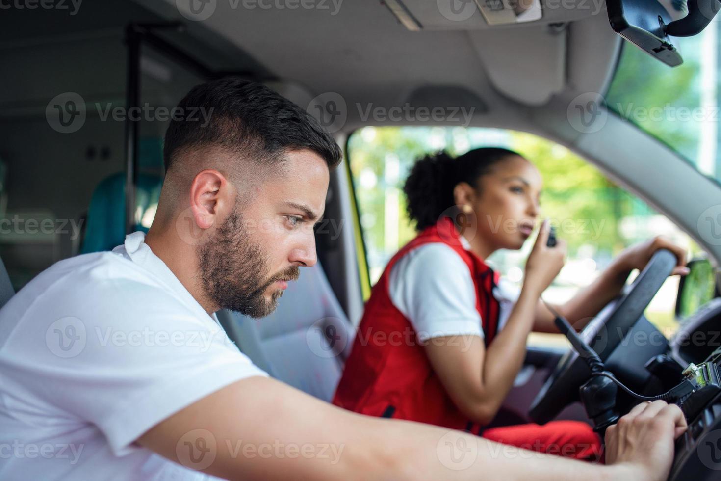 Two paramedics in the front of an ambulance. The focus is on the man, a young man in his 20s looking through the open driver's side window. photo