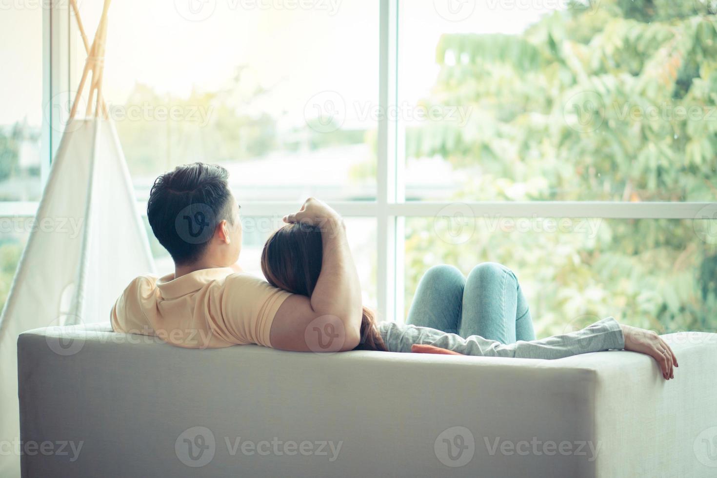 feliz pareja sentada en el sofá y siendo un hombre abrazando a su novia con amor en la sala de estar y relajarse. concepto de romántico en el día de san valentín. propuesta y matrimonio foto