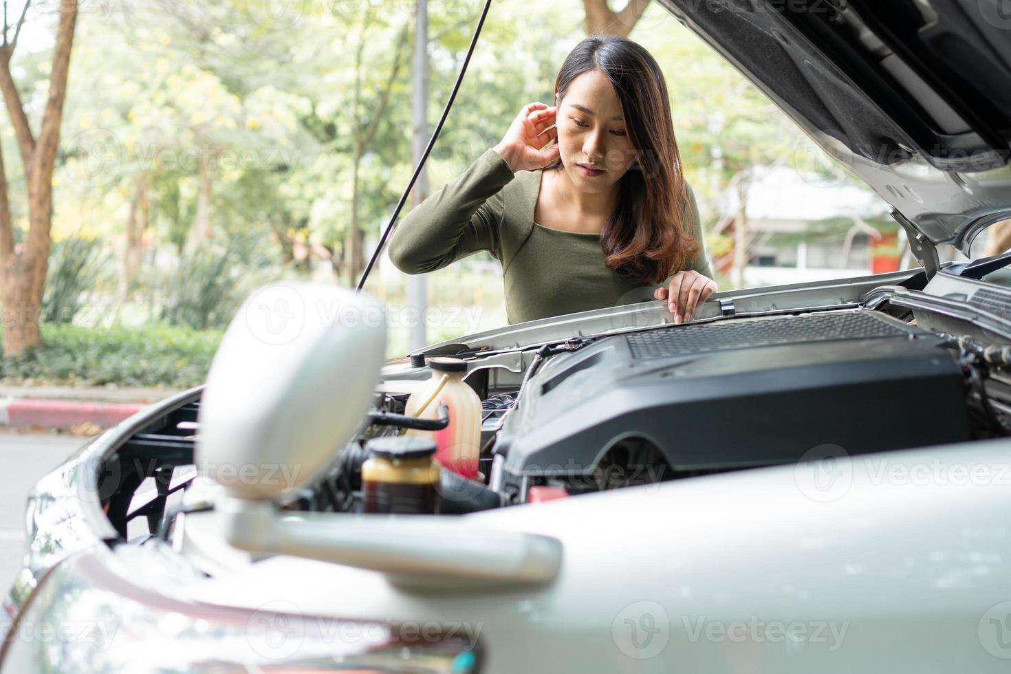 mujer asiática enojada y usando un teléfono móvil pidiendo ayuda después de una avería en el coche en la calle. concepto de problema del motor del vehículo o accidente y ayuda de emergencia de un mecánico profesional foto