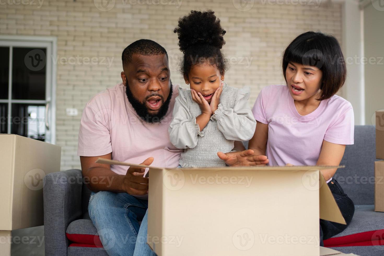 mezclado carrera familias son sentado en el sofá y sorprendido después abierto el regalo caja desde un vecino en el primero día después Moviente casa. concepto de comenzando un nuevo vida para un nuevo familia. foto