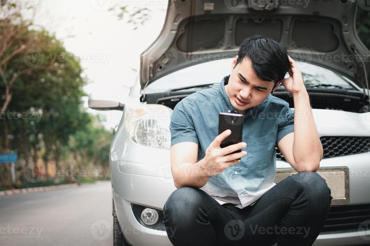 hombre asiático que usa un teléfono móvil para pedir ayuda después de una avería en el coche en la calle. concepto de problema del motor del vehículo o accidente y ayuda de emergencia de un mecánico profesional foto