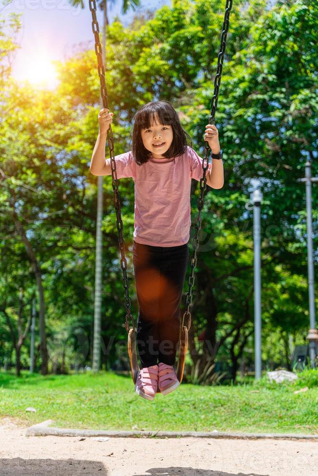 linda pequeño niña teniendo divertido en un columpio en hermosa verano jardín. niño niña jugando en al aire libre patio de recreo en parque. activo verano ocio para niños foto