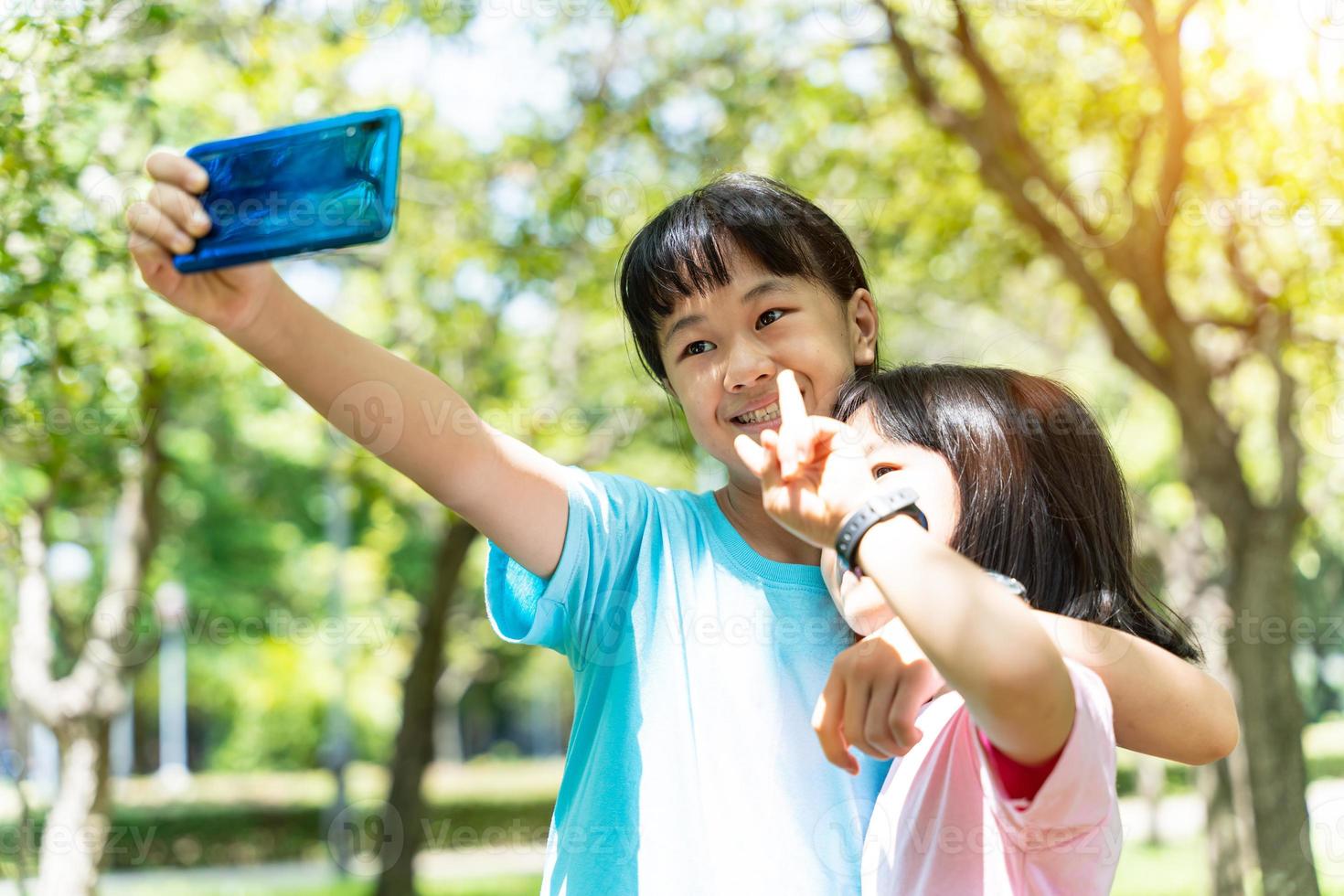 Two sisters hugging while taking selfie with mobile smartphone in the park. Happy friendship family concept. photo