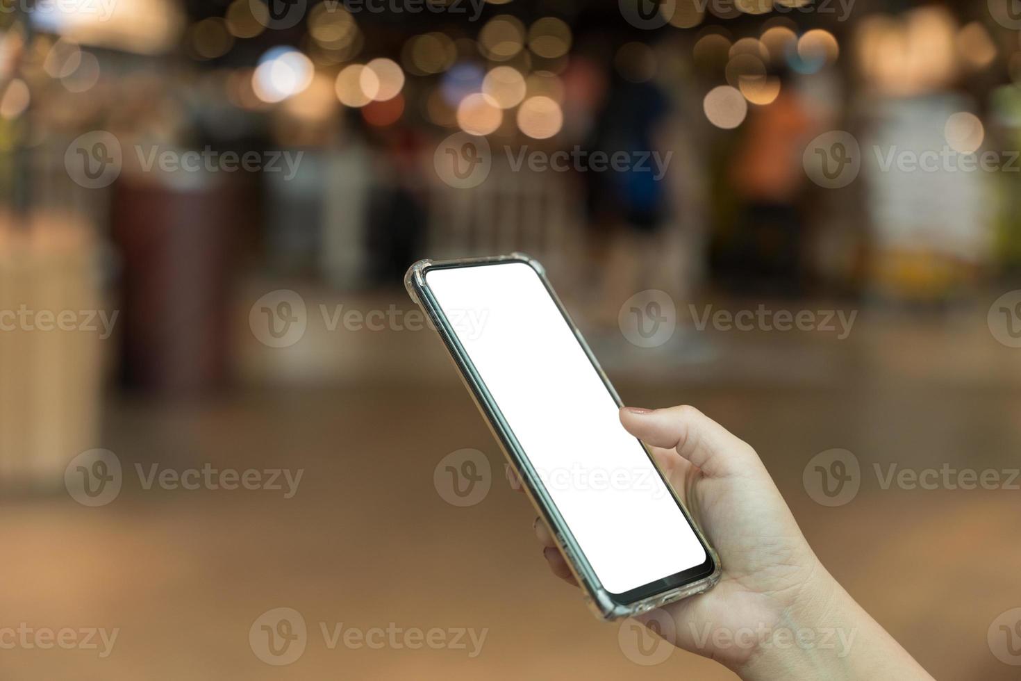 Female hand holding smartphone with blank screen on bokeh light background photo