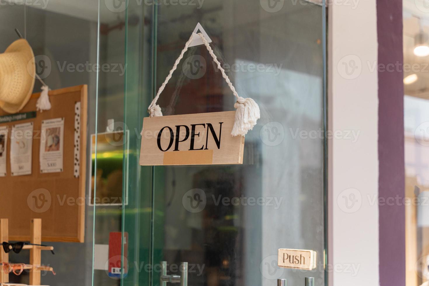 A business sign that says Open on local businesses hang on door at entrance. Say Welcome. Open and closed flip sign in front of shop glass door. photo